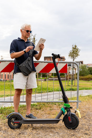 Commuter hipster man with electric scooter using smartphone in the suburbs. eco transport concept 