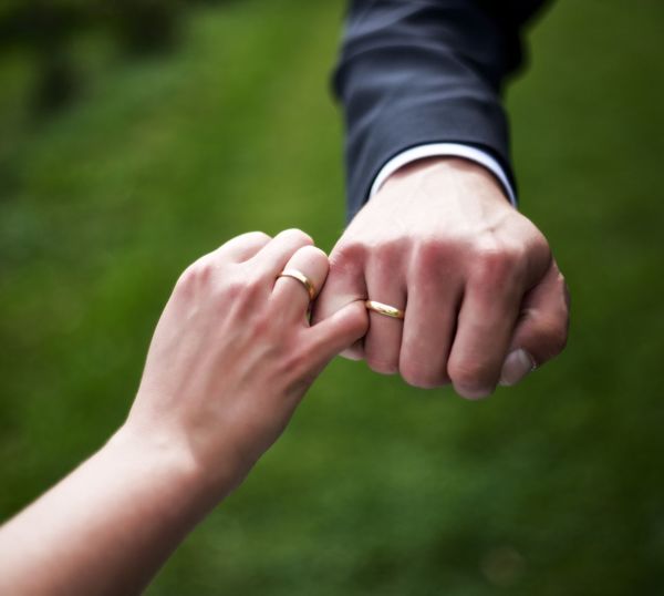 Cropped hands of couple wearing rings holding little fingers