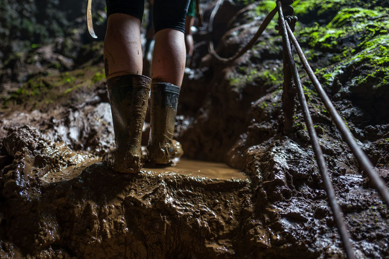 Low section of woman wearing muddy rubber boots while standing on rock in forest