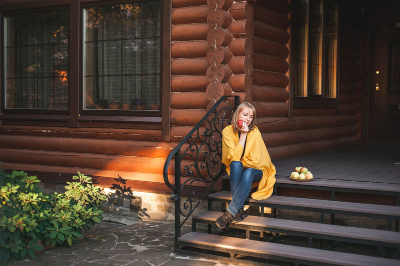 Autumn vibe of relaxation. attractive blonde woman sitting on the porch with ripe apples.