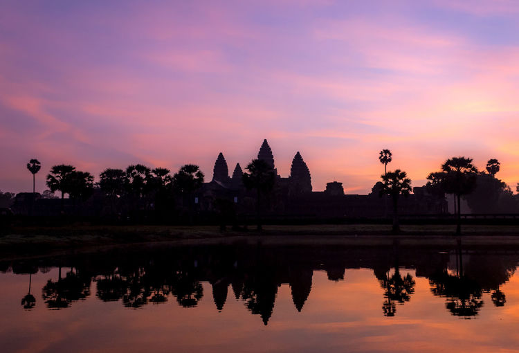 Silhouette trees by angkor wat against cloudy sky during sunset