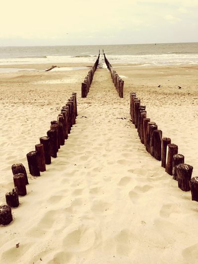 Wooden posts on beach by sea against sky