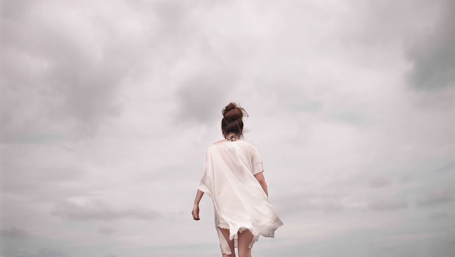 Rear view of woman walking against cloudy sky