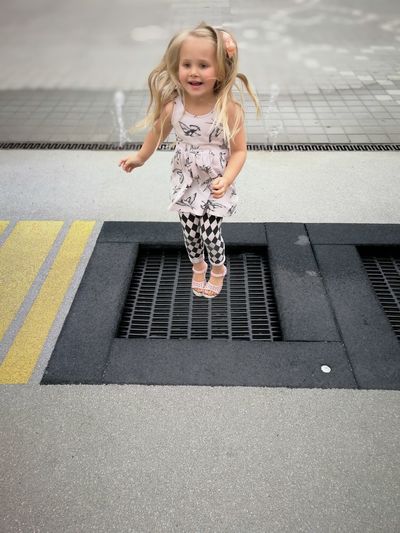Full length of playful girl jumping over metal grate at street