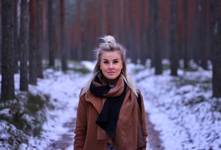 Portrait of smiling young woman standing in forest during winter