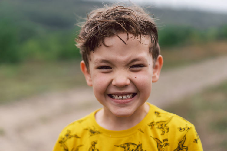 A six year old boy smiles at the camera in the park