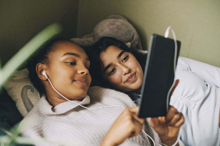 Female teenagers listening music on digital tablet while lying on bed at home