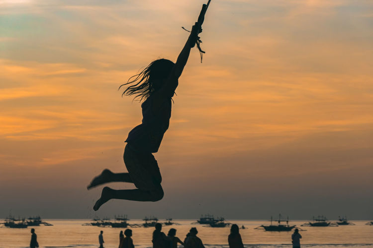 Silhouette woman jumping on beach against sky during sunset