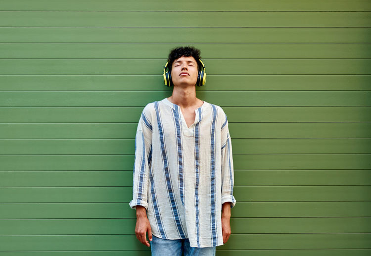 A young afro-haired man listens to music on a green background