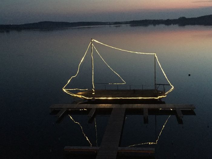 Illuminated boat moored by jetty in lake