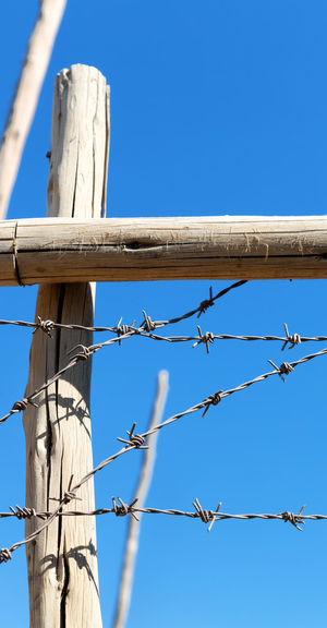 Low angle view of barbed wire fence against blue sky