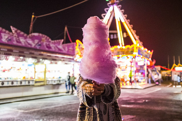 Woman holding cotton candy over face on land in city at night