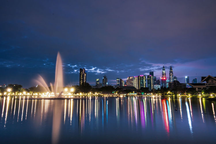Illuminated city by river against lake at night
