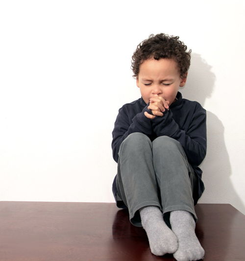 Boy sitting on floor against white background stock photo