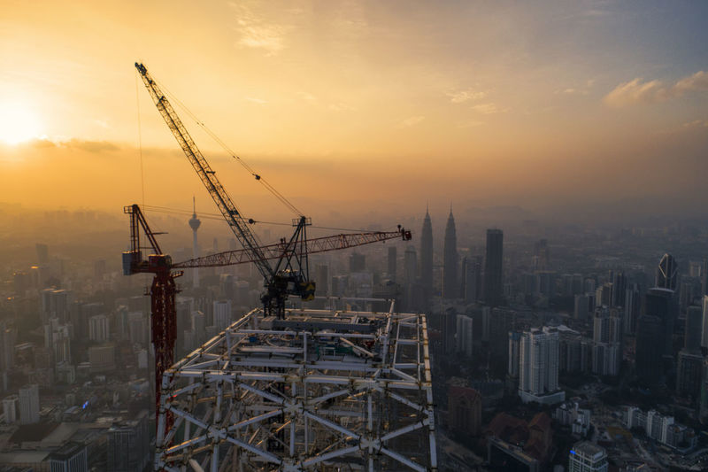 Cranes at construction site in city against sky during sunset