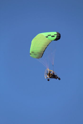Low angle view of people paragliding against clear blue sky
