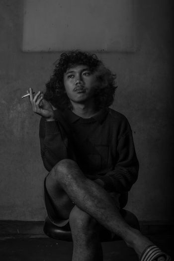 Portrait of man smoking cigarette against wall