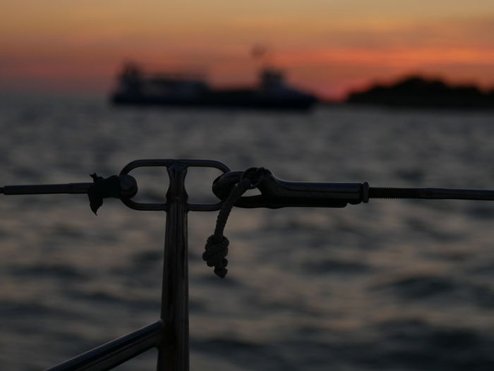 Close-up of metal railing against sea during sunset