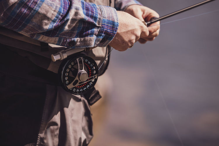 Close-up of fisherman tying fishing rod on waist