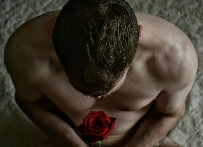 High angle view of shirtless man holding red rose outdoors