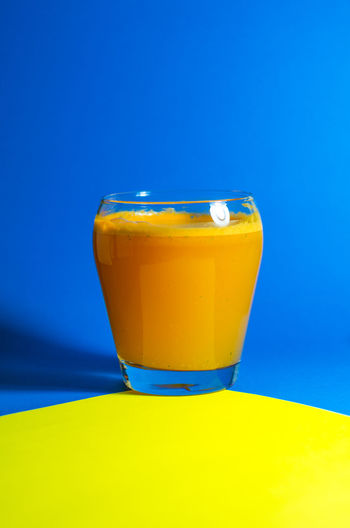 Fruit juice in glass on blue and yellow table