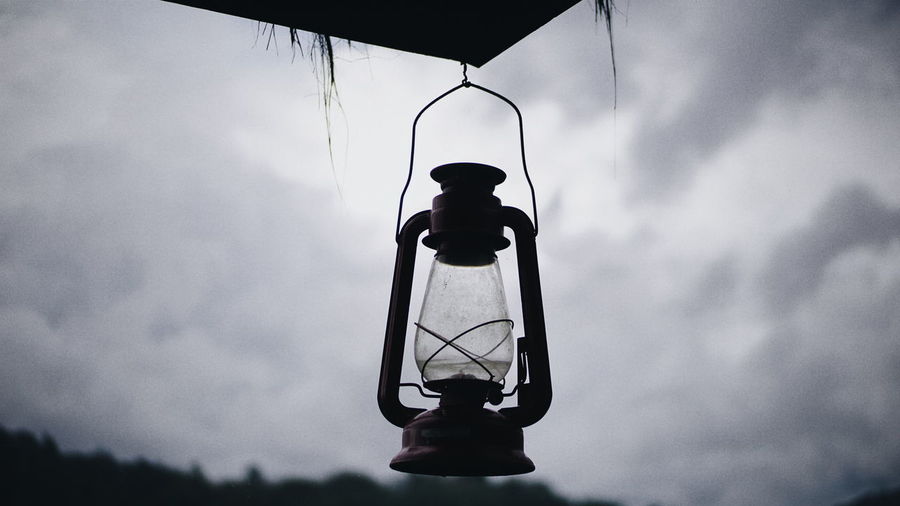 Low angle view of oil lamp hanging against cloudy sky