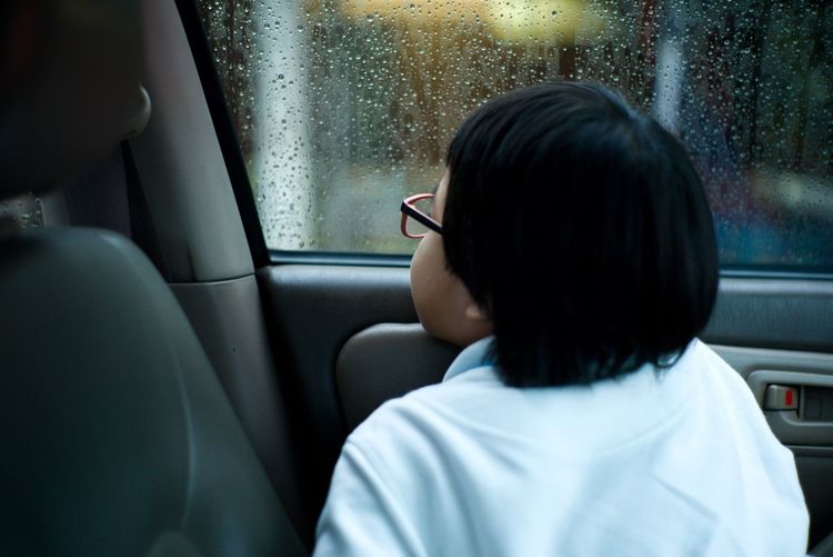 Rear view of girl seen through wet window