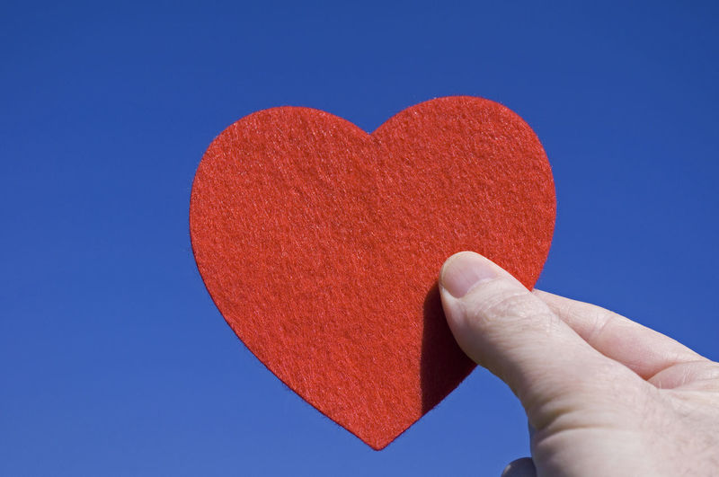 Close-up of hand holding heart shape against blue sky