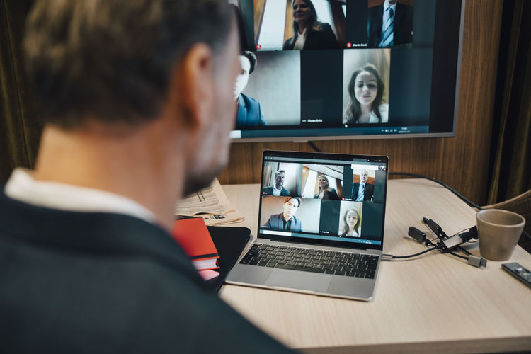 Businessman discussing with colleagues on video call during social distancing in office