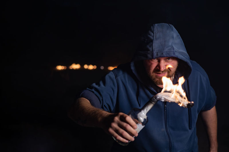 Portrait of man holding molotov cocktail at night