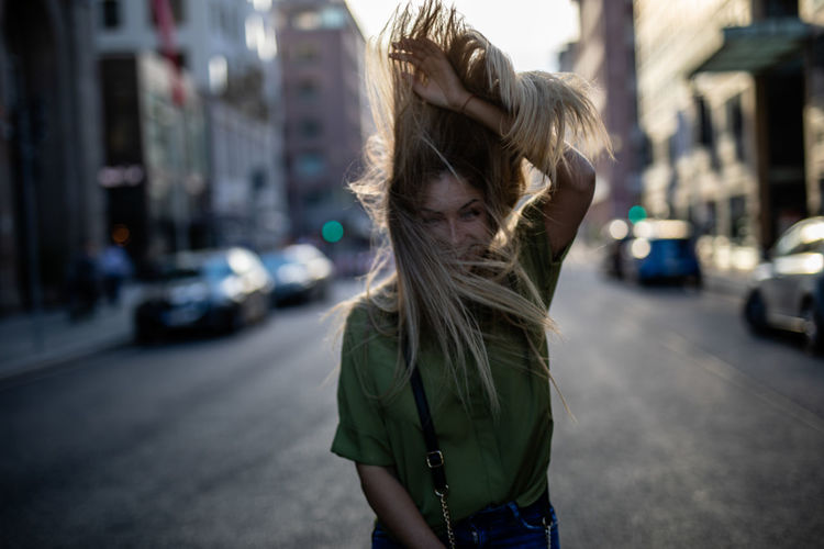 Happy young woman tossing hair while standing on city street