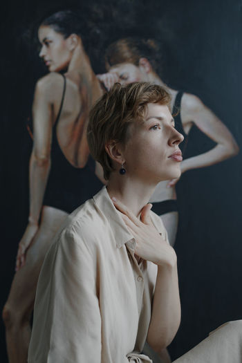 Thoughtful mid adult female artist looking away with hand on neck while sitting by painting