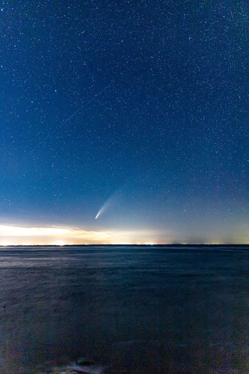 Comet neowise streaking through the starry night sky above the ocean.