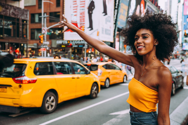 Happy young woman with afro hairstyle hailing a ride on city street