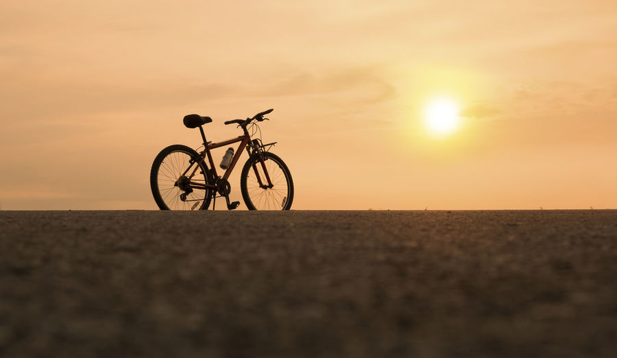 Silhouette bicycle on beach against sky during sunset