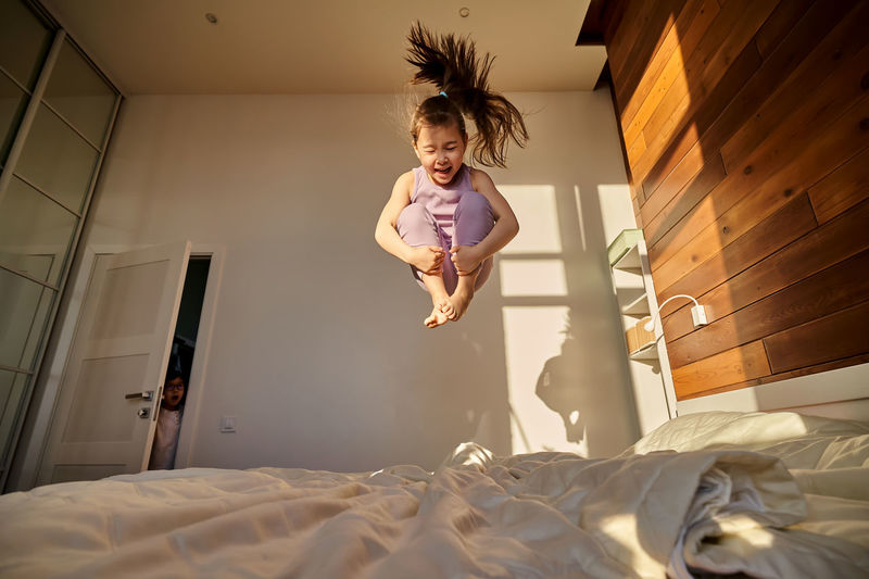 A girl in a purple suit jumps cheerfully on the bed.