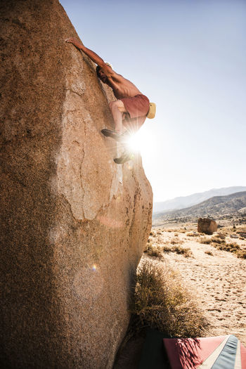 Shirtless man climbing rock against clear sky