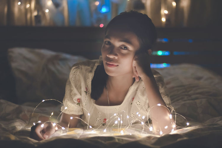 Young woman wore a white lace blouse with led lights on the bed in her bedroom.