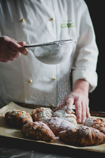 Midsection of chef sprinkling powdered sugar on croissants in bakery