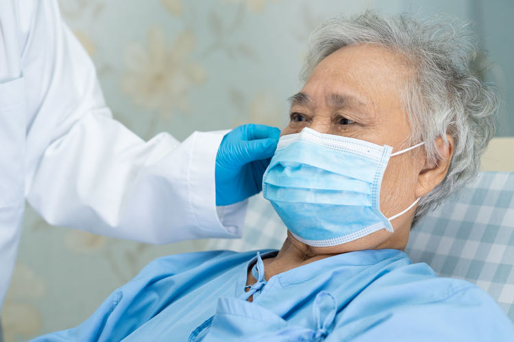 Midsection of doctor wearing mask to senior woman in hospital
