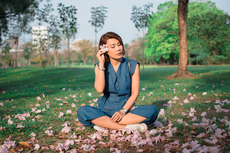Woman holding flowers while sitting on field at park