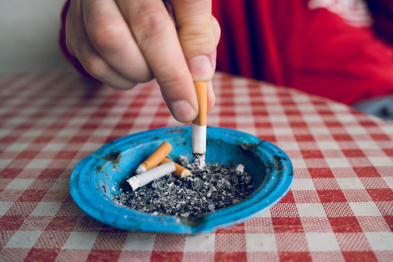 Close-up of hand extinguishing cigarette in ashtray
