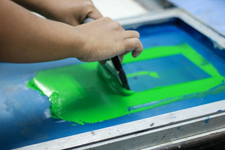 Cropped hands of person applying green ink on silk screen while working at workshop