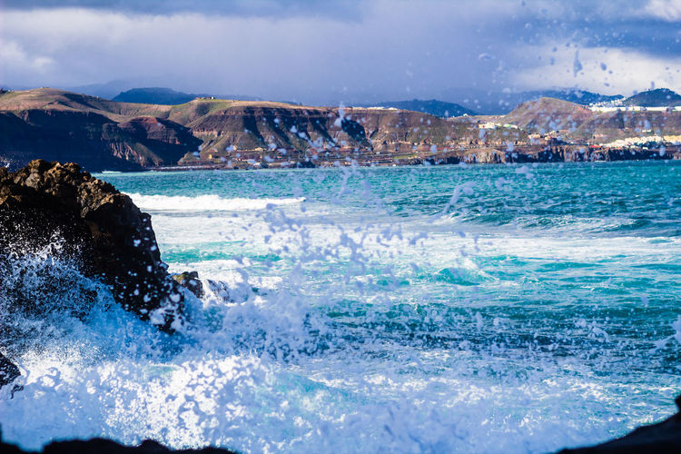 Sea waves splashing on rocks against sky