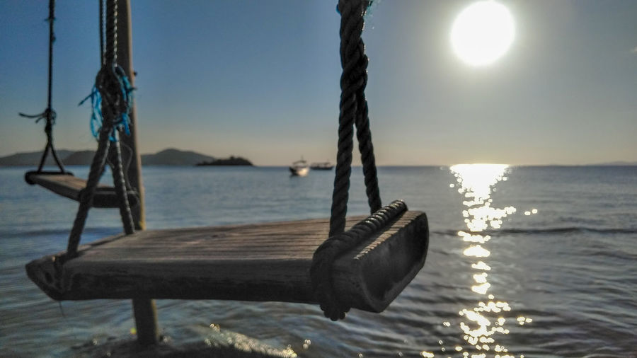 Close-up of swing by sea against sky during sunset