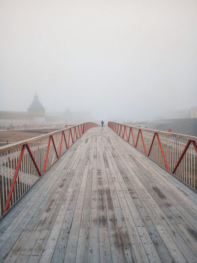 Footbridge over sea against sky during foggy weather