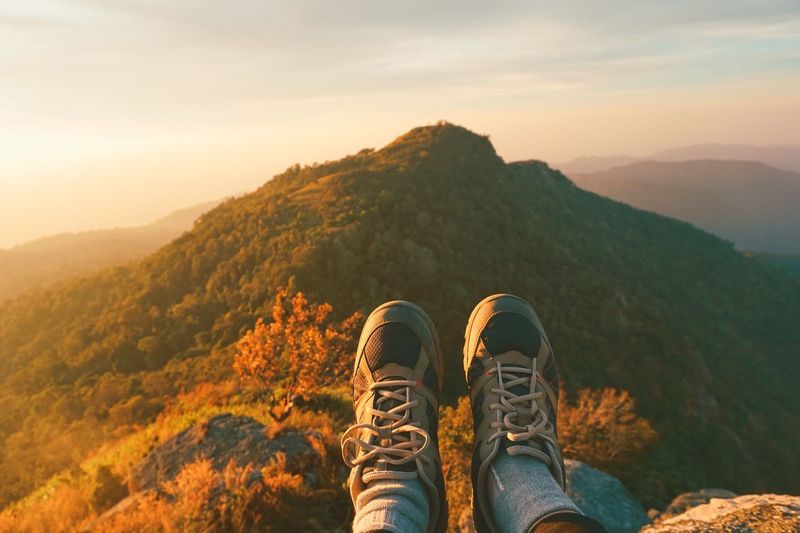Low section of man on mountain against sky during sunset
