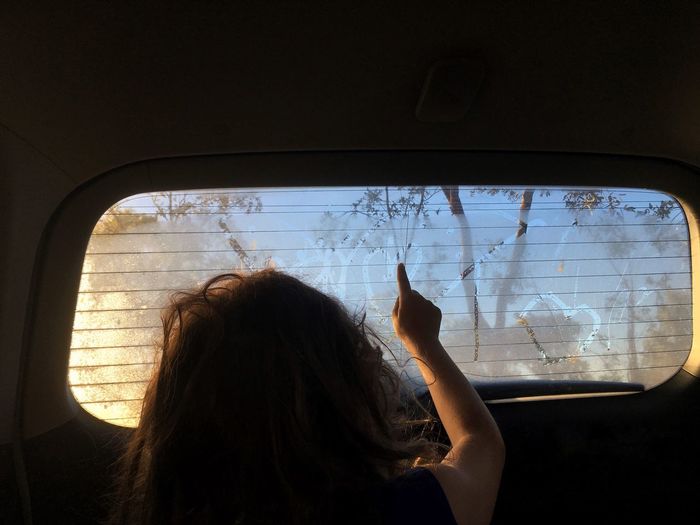 Girl drawing on rear windshield while sitting in car