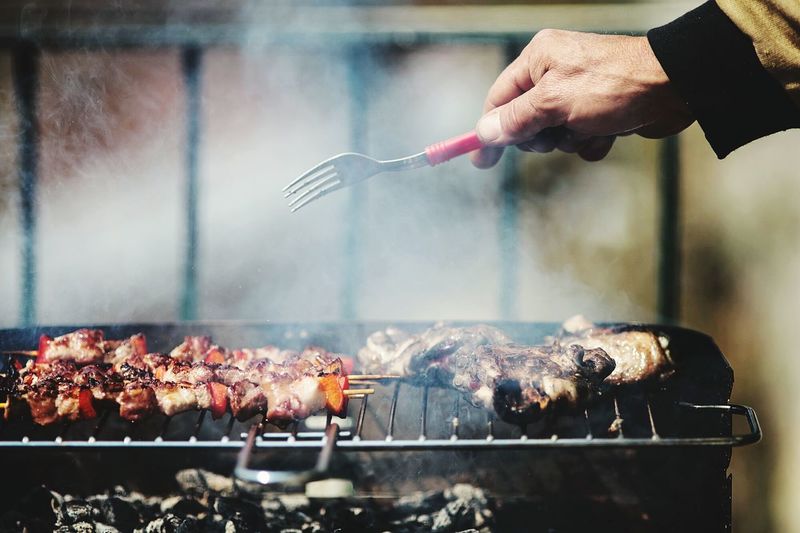 Hand holding fork while grilling meat