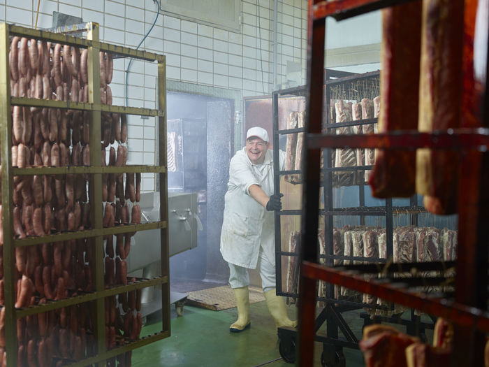 Cheerful butcher working in smokehouse at factory
